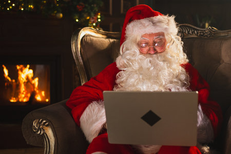 Merry Christmas. Santa Claus with laptop reading letters from children typing buying presents gifts online. Santa with computer on Christmas eve. Mail gifts of Santa Claus. Winter Holiday Celebrationsの写真素材