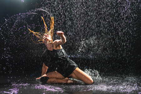 Contemporary woman dancer posing in rain water on black background. Female artist performer dancing with expression. Modern ballerina dancing in darkness. Passion dance in dark. Flexibility balanceの写真素材