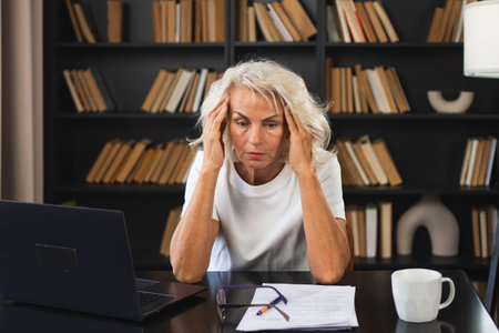Headache pain. Middle aged woman touching temples experiencing stress. Mature old lady tired of work feeling headache sick rubbing temples forehead. Long laptop usage computer vision office syndromeの写真素材