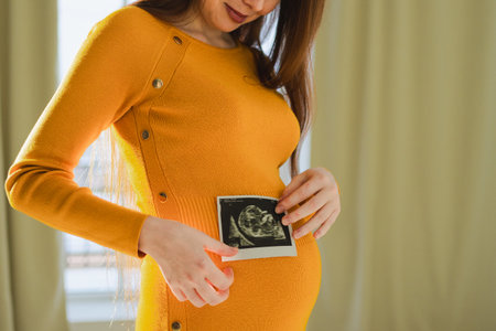 Prenatal ultrasound screening. Pregnant woman hands holding sonogram picture of unborn baby inside...