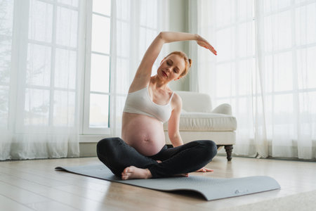 Pregnancy yoga fitness workout training. Pregnant woman practicing yoga at home. Pregnant girl doing sports exercise on yoga mat indoor. Woman with big belly have fitness training practicing asanaの写真素材
