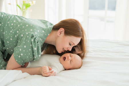 Happy family at home. Mother playing with little toddler child on bed. Mom baby relax playing having...