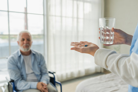 Nurse giving glass water for old man patient in wheelchair. Man in chair for people with disability drinking fresh water. Senior man and nurse at homeの写真素材