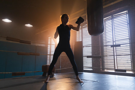 Women self defense girl power. Strong woman fighter training punches on boxing ring. Healthy strong girl punching boxing bag. Training day in boxing gym. Strength fit body workout trainingの写真素材