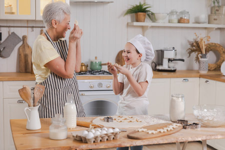 Happy family in kitchen. Grandmother granddaughter child cutting cookies of dough on kitchen table together. Grandma teaching kid girl cook bake cookies. Household teamwork helping family generationsの写真素材