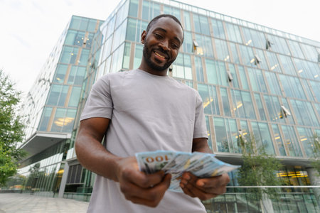 African American man holding money dollar bills on urban street in city. Businessman guy counting...
