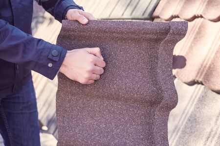 Sheet of polymer roof tiles. A worker holds a sheet of polymer plastic tile and bangs on it with his fist.の写真素材
