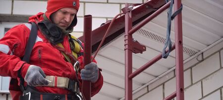 Moscow, Russia - February 15, 2019: Worker does the installation of the roof of the house. Installation of metal tiles, snow retainers and other elements of the roof.のeditorial素材