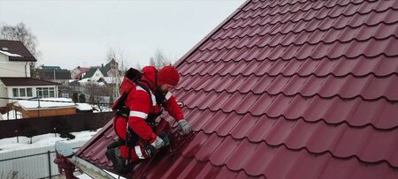 Moscow, Russia - February 15, 2019: Worker does the installation of the roof of the house. Installation of metal tiles, snow retainers and other elements of the roof.のeditorial素材