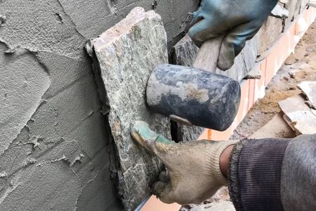 A builder faces the basement of a house with a wild stone. Flat for cladding, tabata on the construction site.の写真素材
