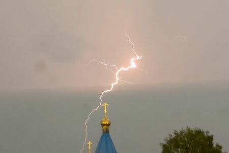 Lightning during a thunderstorm in the sky above the dome and cross of the church. Natural phenomenon of electricity, lightning.の写真素材