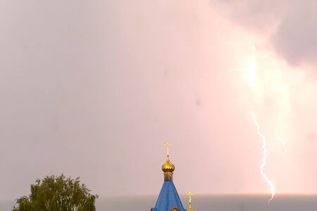 Lightning during a thunderstorm in the sky above the dome and cross of the church. Natural phenomenon of electricity, lightning.の写真素材