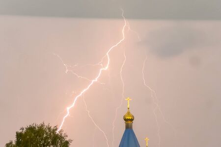 Lightning during a thunderstorm in the sky above the dome and cross of the church. Natural phenomenon of electricity, lightning.の写真素材