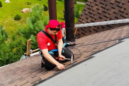 Moscow, Russia - August 21, 2019: Worker does the installation of the roof of the house. Installation of metal tiles, snow retainers and other elements of the roof.の写真素材