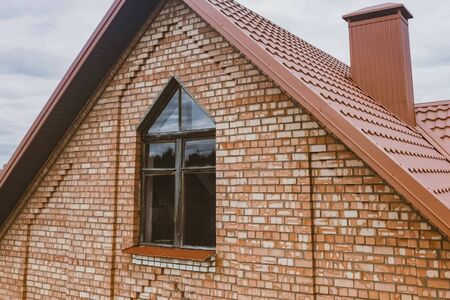 Modern roof made of metal. Corrugated metal roof and metal roofing. Beautiful pink brick brick house and orange roof.の写真素材