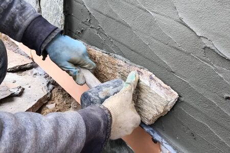 A builder faces the basement of a house with a wild stone. Flat for cladding, tabata on the construction site.の写真素材