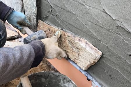 A builder faces the basement of a house with a wild stone. Flat for cladding, tabata on the construction site.の写真素材