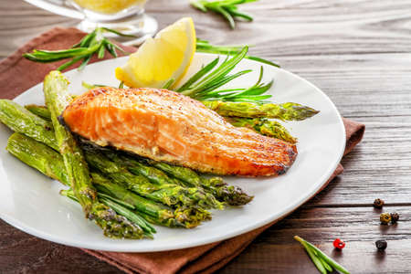 Delicious baked salmon with lemon, asparagus and spices on white plate on wooden background.の写真素材