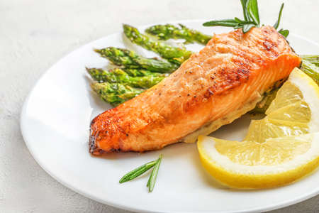 Delicious baked salmon with lemon, asparagus and spices on white plate on white background.の写真素材