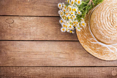 Chamomile bouquet and women's straw hat on wooden background. Top view. Copy space.