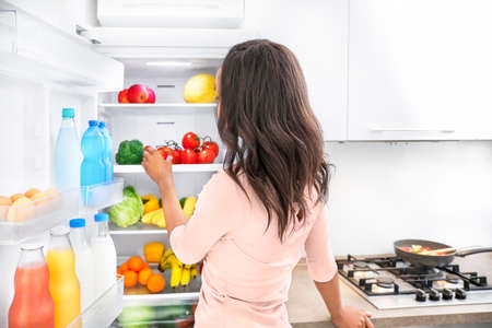 Young african woman choosing products in fridge in kitchen. Healthy food concept.の写真素材