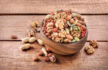 Mixed nuts in wooden bowl on wooden background.