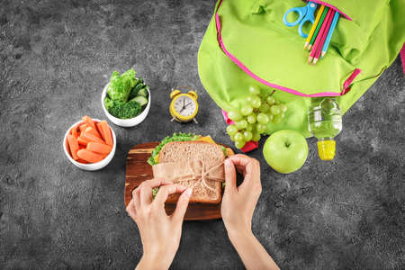 Mum's hands preparing school lunch for child on black chalkboard background. Top view.