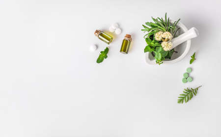 Medicinal herbs in mortar with pestle, organic essential aroma oil in glass bottles and herbal pills isolated on white background. Top view. Copy space. Herbal medicine concept.の写真素材