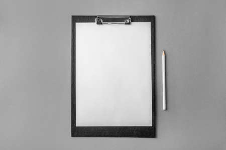 Black clipboard with blank white sheet and white pencil on gray background. Top view.の写真素材