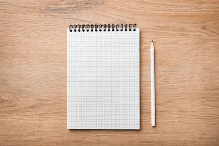 Blank spiral notebook and white pencil on wooden background. Top view. Copy space.