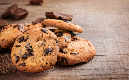 Chocolate chip cookies and chocolate pieces on wooden background.