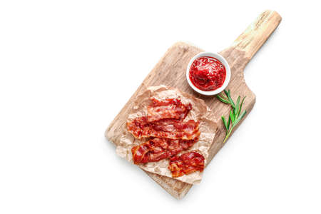 Fried crispy bacon slices, rosemary sprigs and tomato sauce in small bowl on white background. Top...