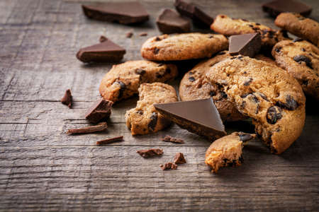 Chocolate chip cookies and chocolate pieces on wooden background.