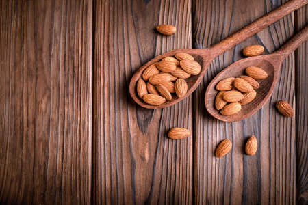 Almond nuts in wooden spoons on wooden background.の写真素材