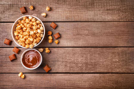 Sweet caramel popcorn and melted caramel on wooden background. Top view. Copy space.の写真素材