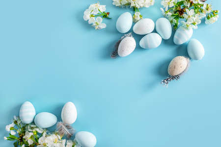 Pastel colored Easter eggs and spring blooming branches on blue background. Top view.