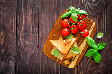 Toast bread slices, cherry tomatoes and basil leaves on wooden background. Top view. Copy space.の写真素材