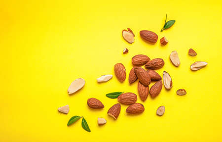Whole and halved almond nuts with leaves on yellow background. Top view. Copy space.