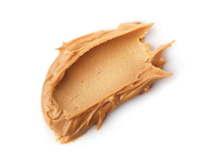 Glass jar and spoon full of crunchy peanut butter with peanuts in nutshell nearby on wooden...