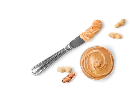 Glass jar and spoon full of crunchy peanut butter with peanuts in nutshell nearby on wooden background. Copy space.の写真素材