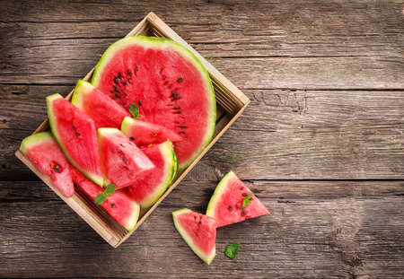 Ripe juicy watermelon pieces in box on wooden background. Top view.の写真素材
