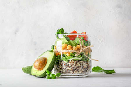 Healthy homemade salad in glass jar with quinoa, vegetables and herbs om white background. Vegan food concept.の写真素材