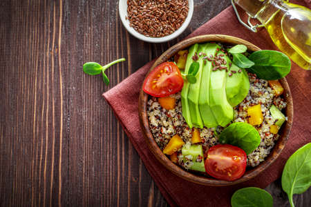 Healthy vegetarian lunch bowl with quinoa, avocado, tomatoes, spinach and seeds on wooden background. Top view.の写真素材