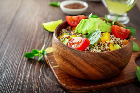 Healthy vegetarian lunch bowl with quinoa, avocado, tomatoes, spinach and seeds on wooden background.の写真素材