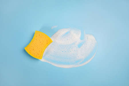 hand in a yellow rubber glove washes the wall with an orange soft rag, cleaning and washing the walls, blue background copy space, cleaning concept, spring cleaning, housework conceptの写真素材