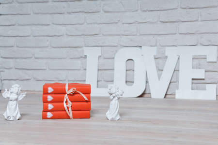 Two white angels with a violin on red books against a white brick wall with the word Love. High quality photoの写真素材