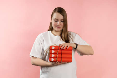 Clever young girl with pack of red books and brown hair in a white t-shirt on a pink background....
