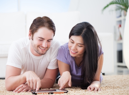 Lovely couple lying on carpet in living room and watching their favorite show on tablet pc.の写真素材