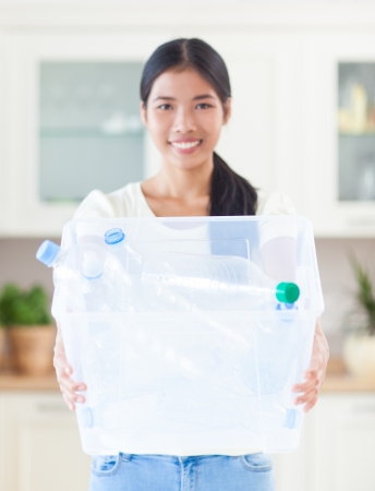 A beautiful Asian woman holding a crate full of bottles for recycling.の写真素材