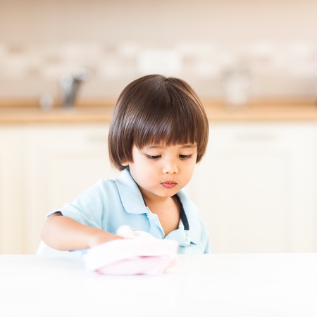 A cute little boy cleaning the counter top in the kitchen.の写真素材